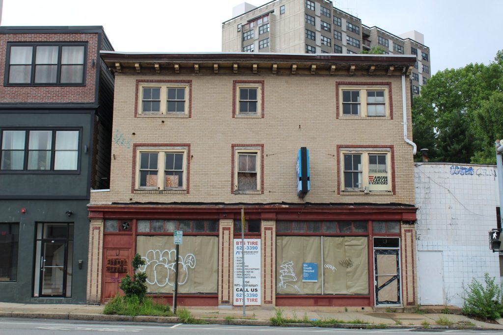 Abandoned building with boarded windows, graffiti, and a tire shop sign on the ground floor.