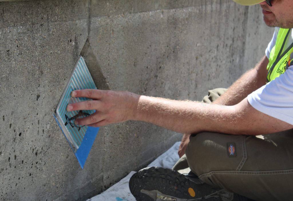 A person in work attire applies a tool to a concrete wall, focusing on a specific area.
