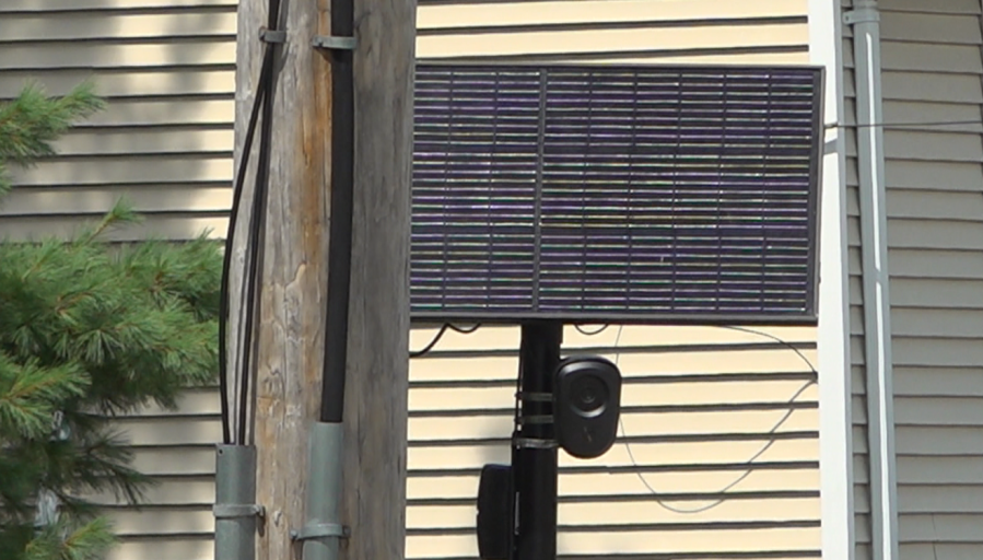 A solar panel mounted on a pole, with wires connected to nearby structures.