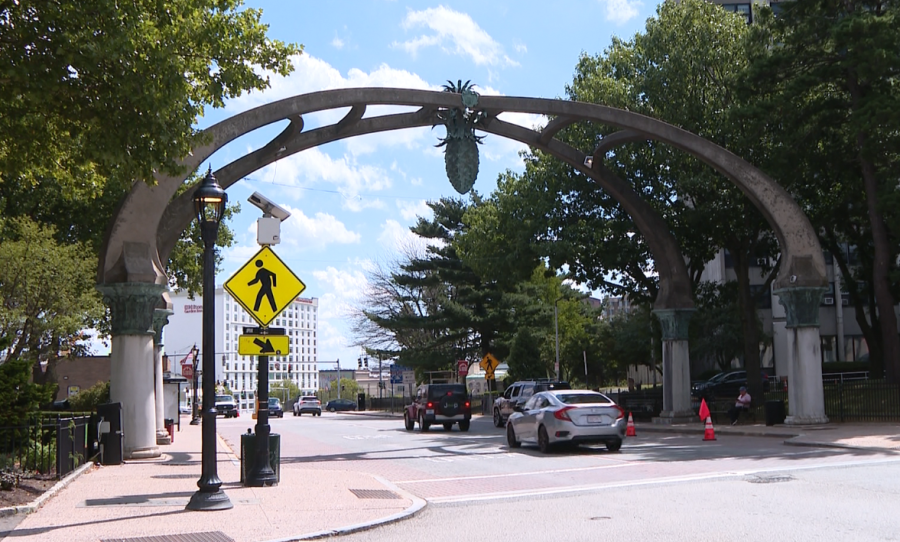 A decorative archway with a pineapple design spans a street, surrounded by trees and vehicles.