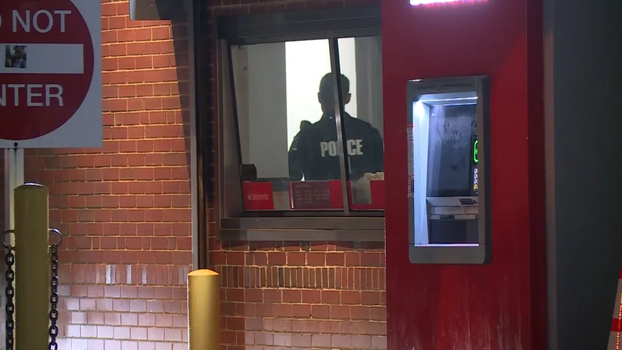 Police officer stands at a bank window, with an ATM visible nearby and a "Do Not Enter" sign in the foreground.