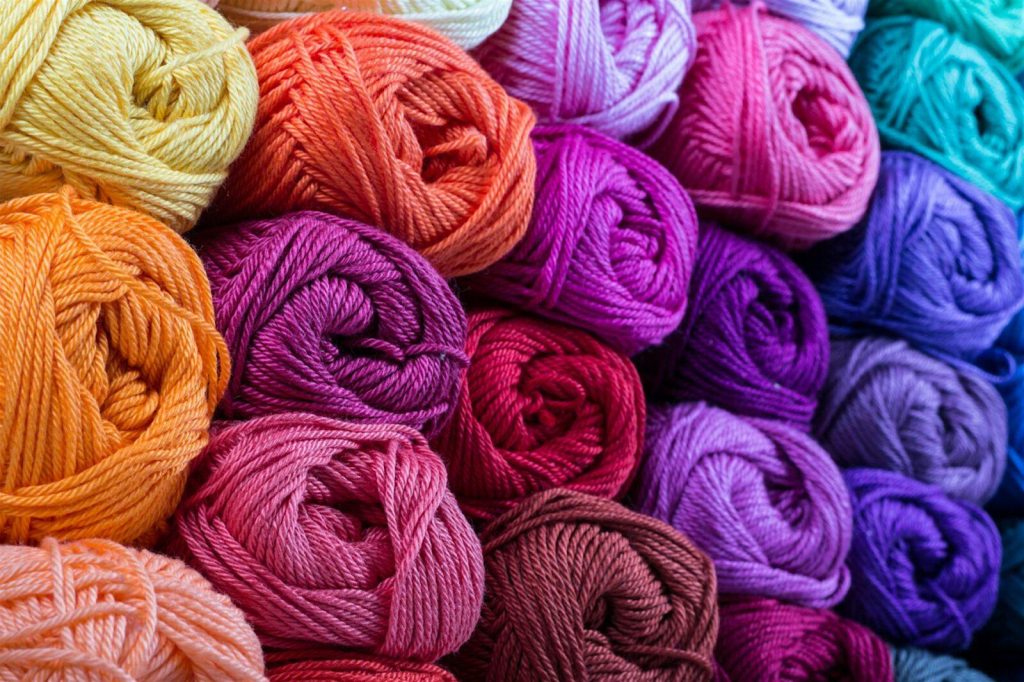 Colorful yarn balls in various shades of orange, pink, purple, and blue stacked together.