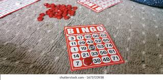 Bingo cards and red markers are scattered on a textured surface, with one card prominently displayed.