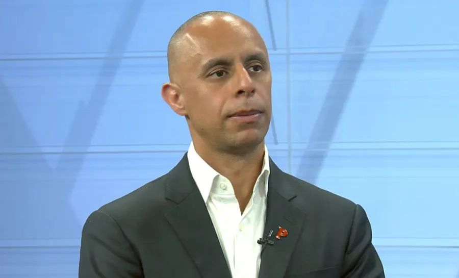 A man in a suit listens attentively during a discussion, with a neutral expression.
