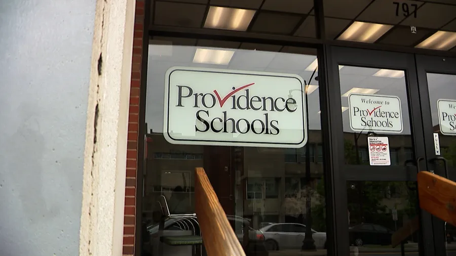 Sign for Providence Schools displayed on a glass door, with a wooden railing in the foreground.