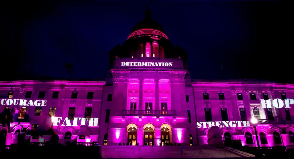 A building illuminated in pink displays words: "Courage," "Faith," "Strength," "Hope," and "Determination.