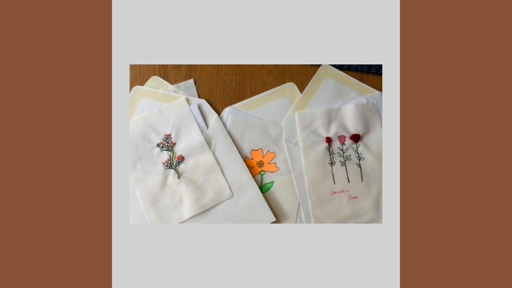 Embroidered cards with floral designs and envelopes arranged on a wooden surface.