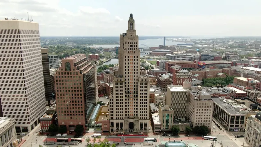 Tall, art deco building stands prominently among modern structures in a city skyline.
