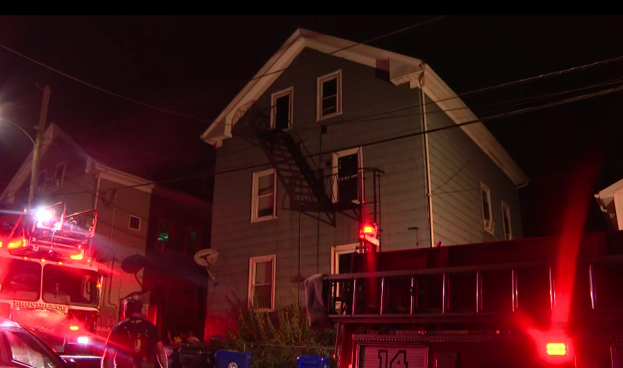 Firefighters respond to a house fire at night, with a fire truck and smoke visible.