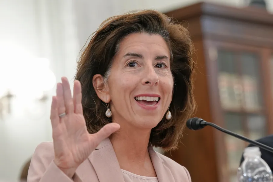 A woman gestures while speaking at a microphone, smiling in a formal setting.