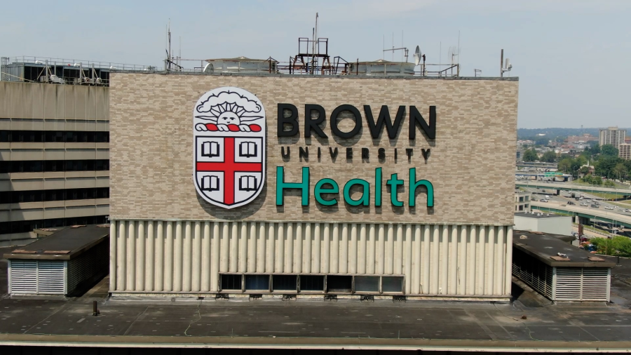 Brown University Health logo displayed prominently on a building facade. Urban landscape visible in the background.