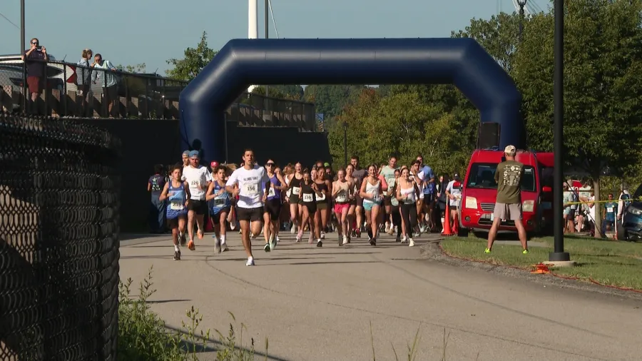 Runners start a race under a large blue arch, with spectators and vehicles in the background.