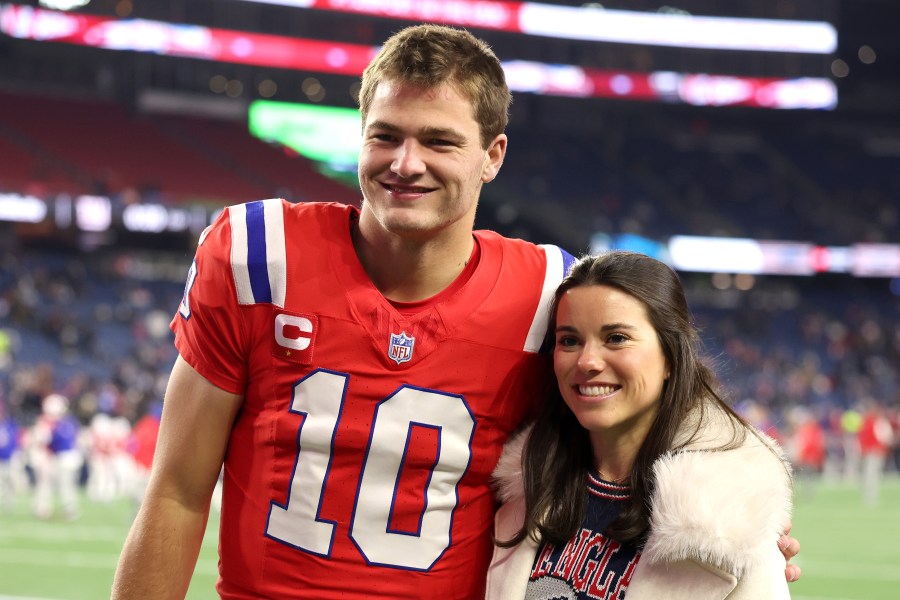 A football player in a red jersey poses with a woman, both smiling on the field after a game.