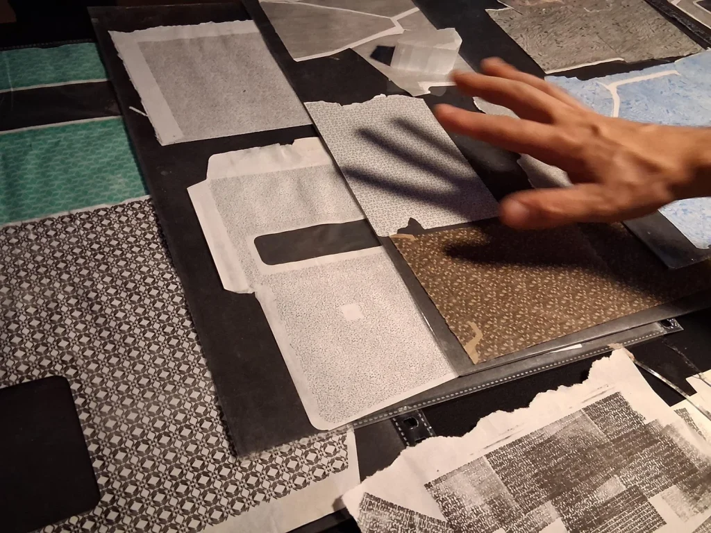A hand gestures over various patterned papers laid out on a table.