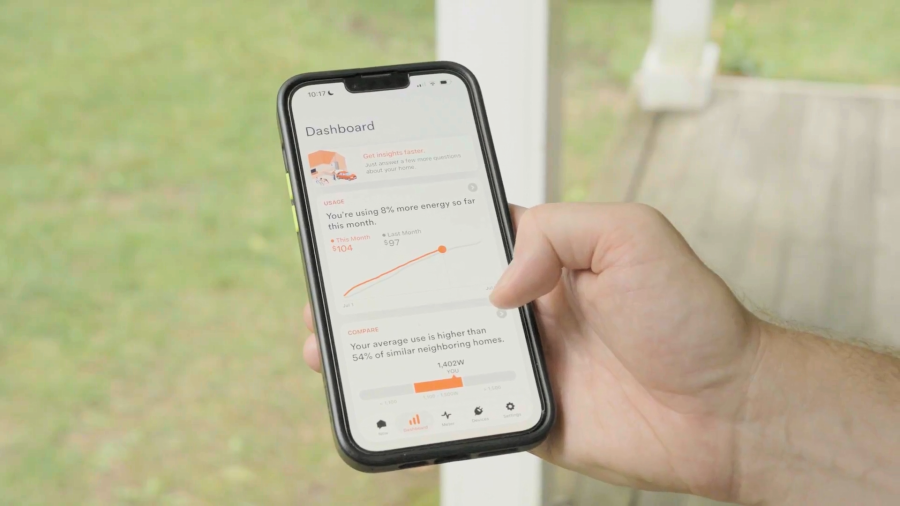 A person holds a smartphone displaying an energy usage dashboard with graphs and comparisons.