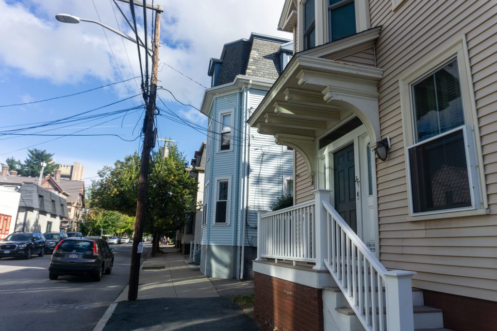 Street view featuring two houses, a power pole, and parked cars along the sidewalk.
