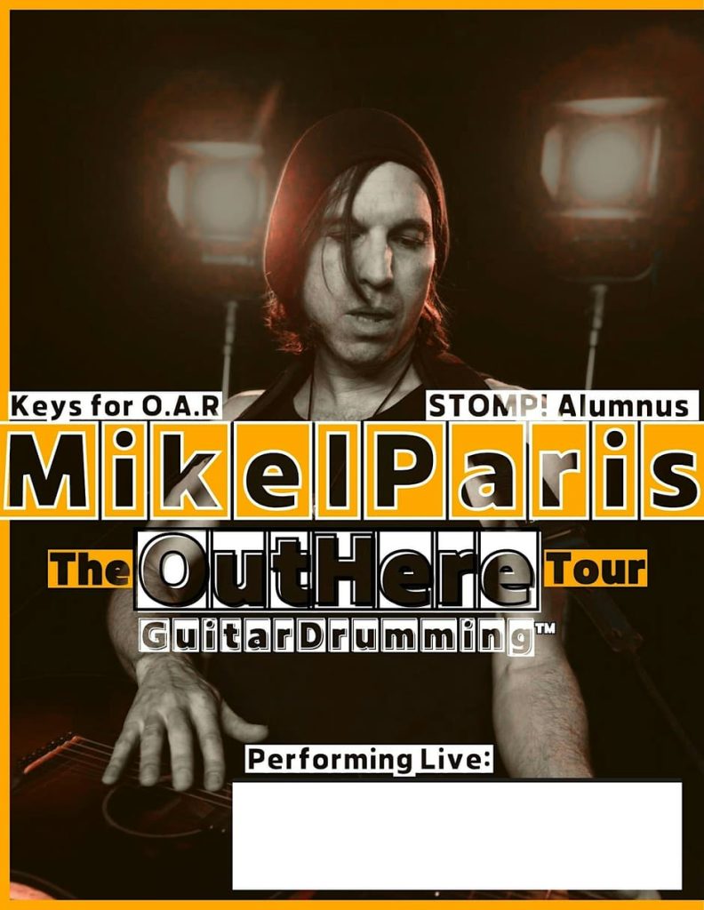 Mikel Paris performs live, showcasing GuitarDrumming™ with dramatic lighting.