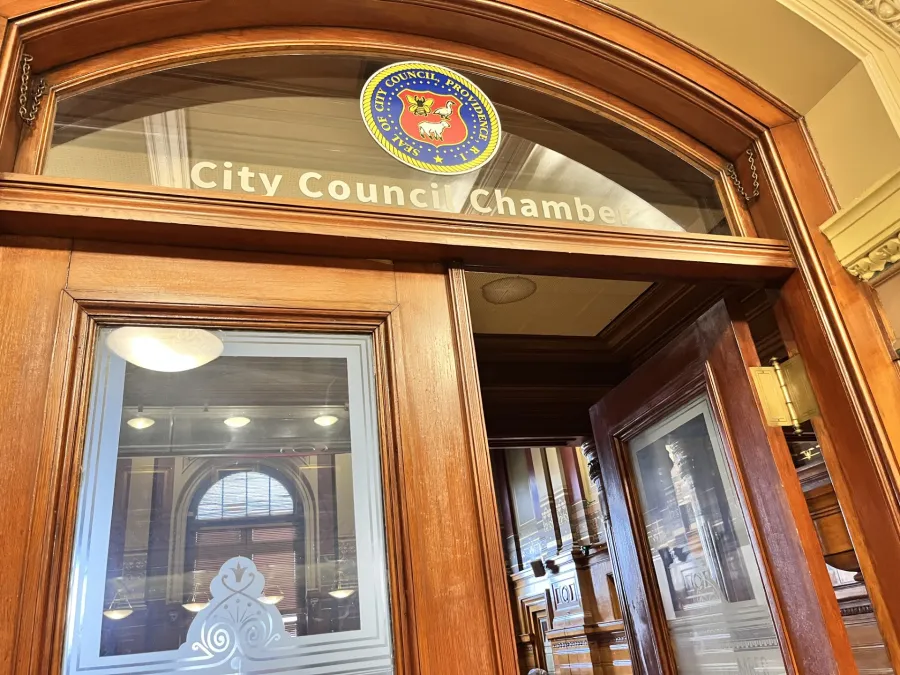Wooden door with "City Council Chambers" sign and city seal, leading into a well-lit meeting room.