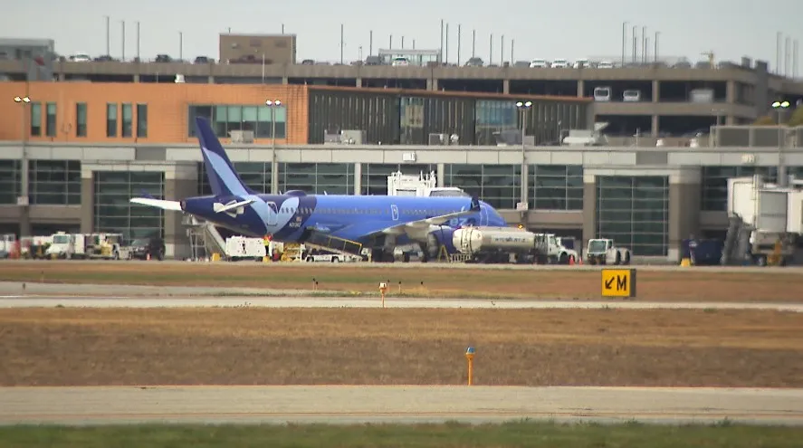 Breeze Airways plane parked at terminal with ground crew and vehicles nearby.
