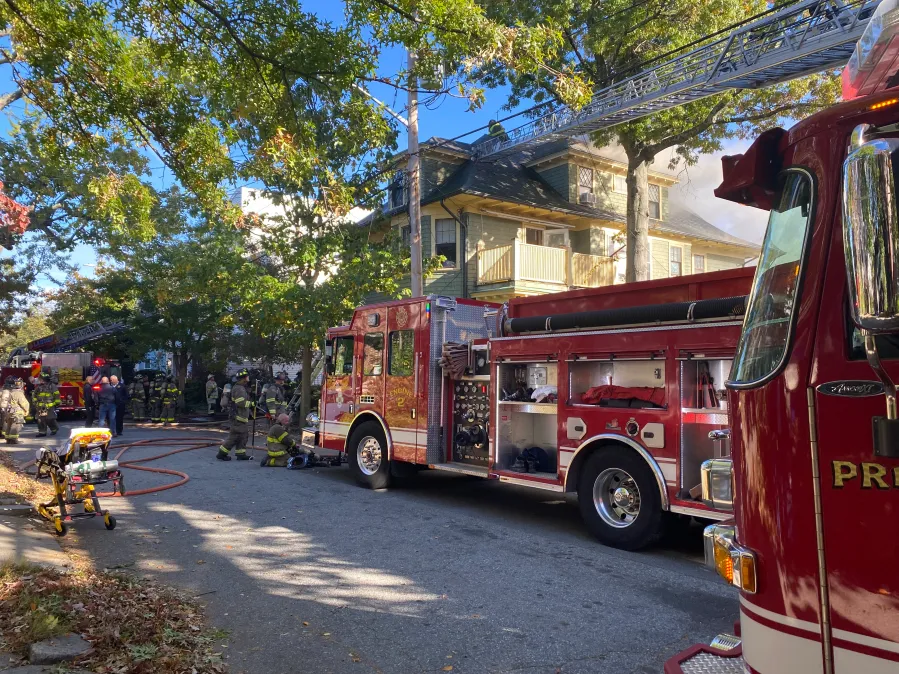 Firefighters respond to a house fire, with a fire truck and equipment visible on the street.