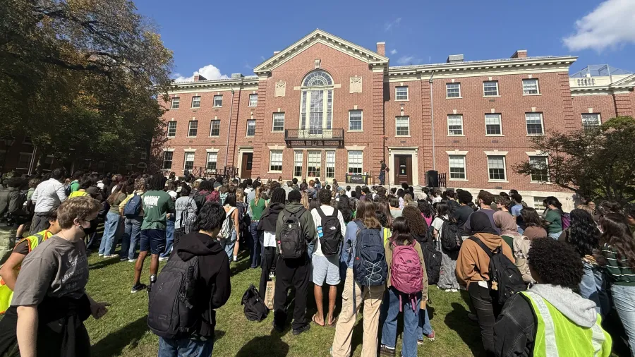 Students gather on a lawn in front of a brick building, listening to a speaker.