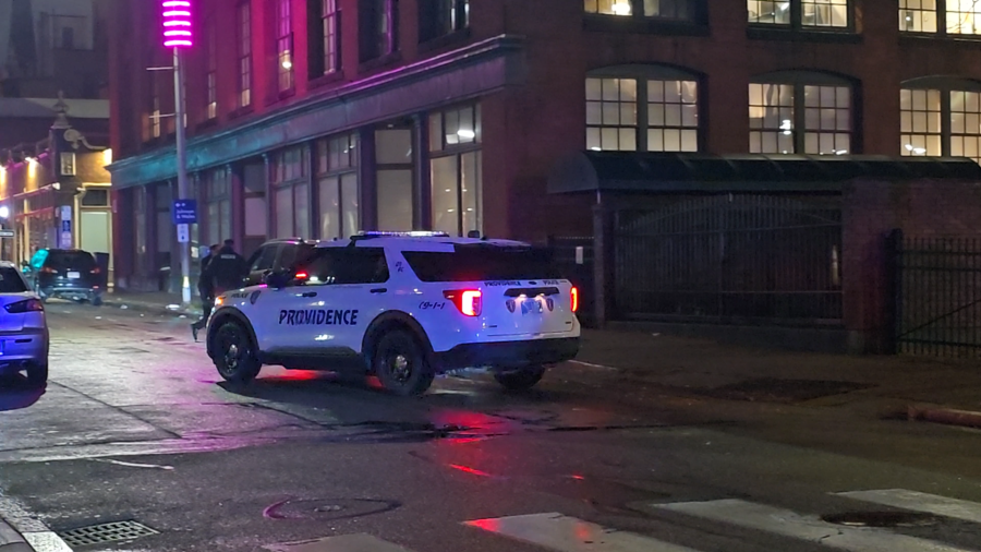 Police vehicle marked "Providence" parked on a wet street, illuminated by nearby neon lights.