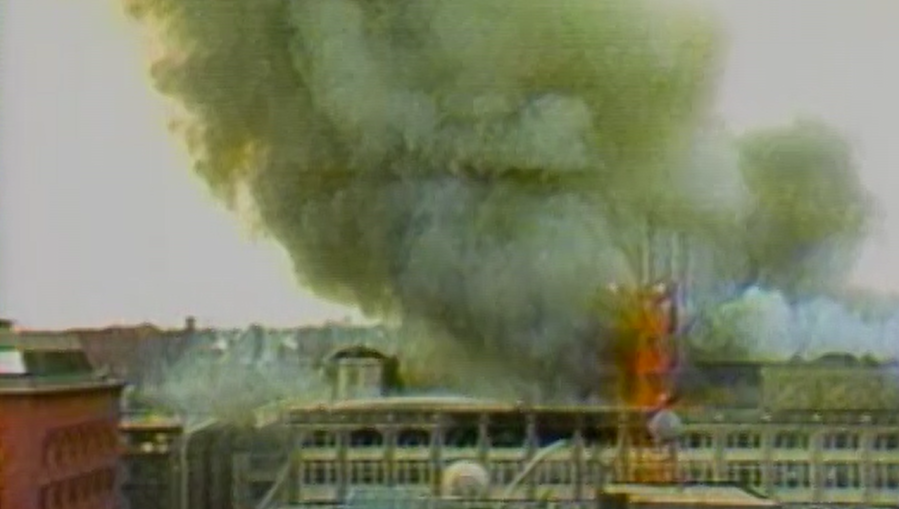Thick smoke billows from a building, with flames visible amidst the destruction.