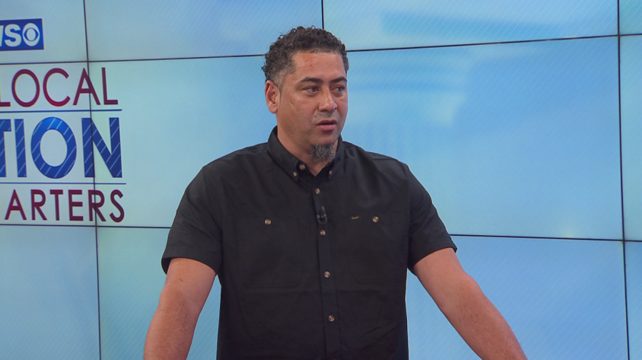 A man in a black shirt speaks in front of a screen displaying "LOCAL ACTION STARTERS.