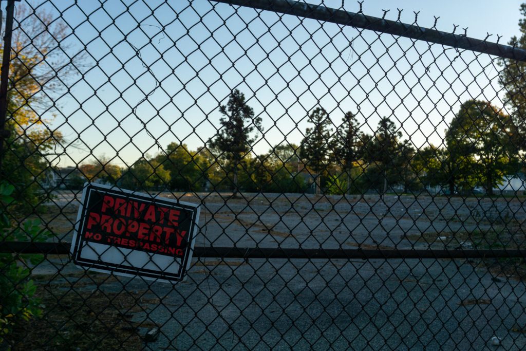 A chain-link fence encloses an empty lot with a "Private Property" sign visible. Trees line the background.