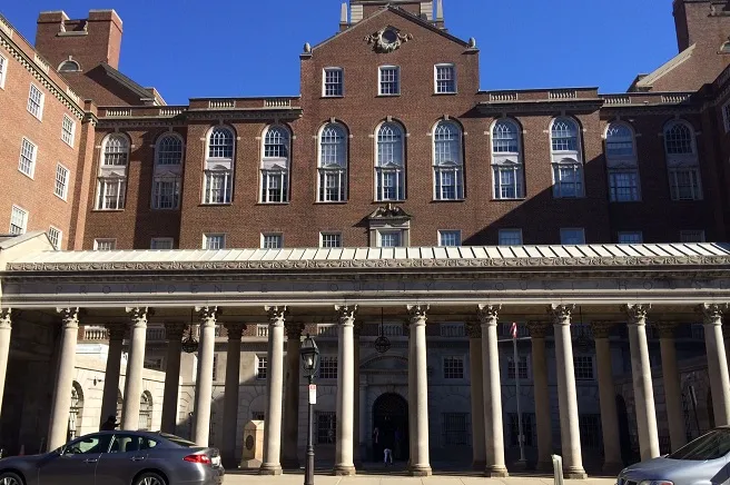 Historic brick building with a colonnade and large windows, set against a clear blue sky.