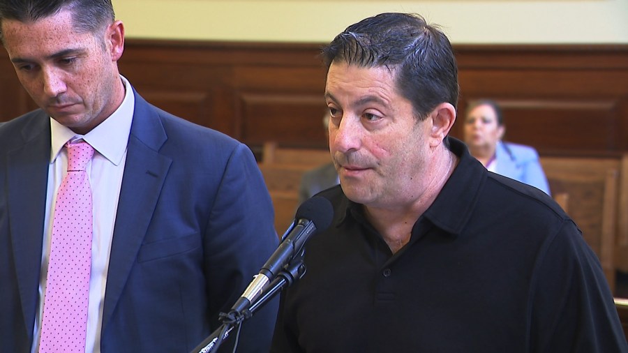 A man speaks into a microphone while another man listens attentively in a courtroom setting.